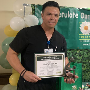 uci health daisy award winner nick turmarao accepting his award and holding the healer's statue