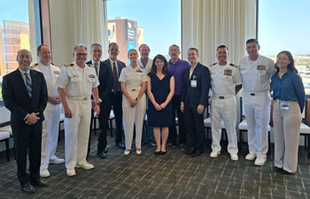 uci health president and ceo chad t lefteris in a suit, left, stands with us navy officers in ceremonial dress in a conference room with uci medical center in the background