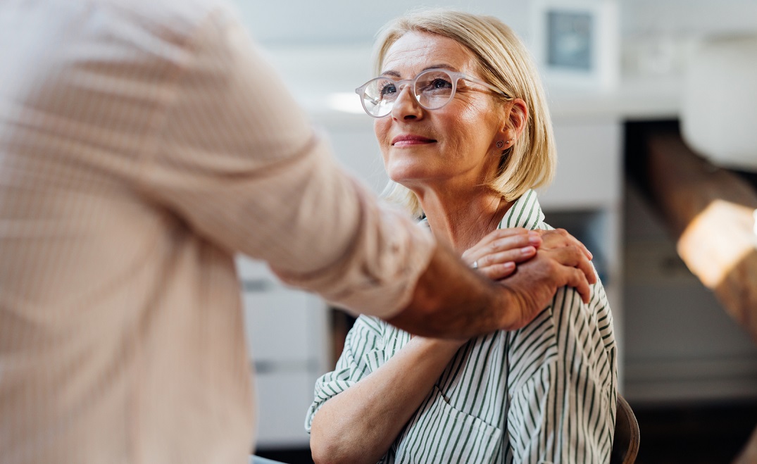 A blond senior woman receives comfort by a hand on her shoulder