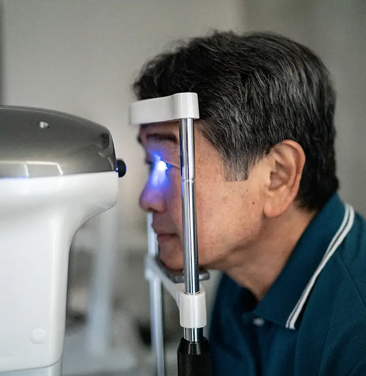 Person undergoing an eye test at an exam machine with blue light shining on their eye.